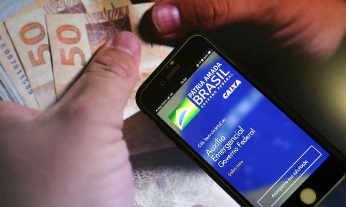 #Pracegover Foto: na imagem há duas mãos, um celular e cédulas de dinheiro