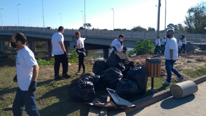 #Pracegover Foto: na imagem há pessoas, uma ponte, árvores e sacos de lixo