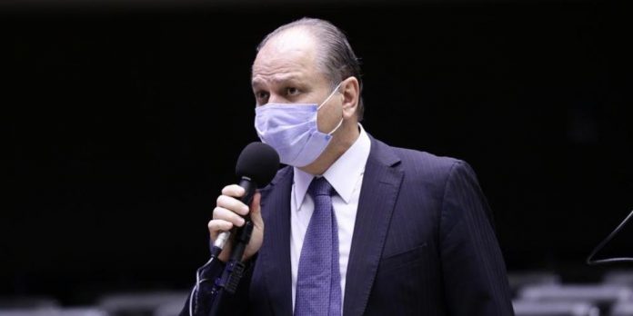 #Pracegover foto: na imagem há um homem de máscara, terno e microfone