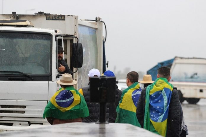#Pracegover foto: na imagem há pessoas com a bandeira do Brasil e um caminhão