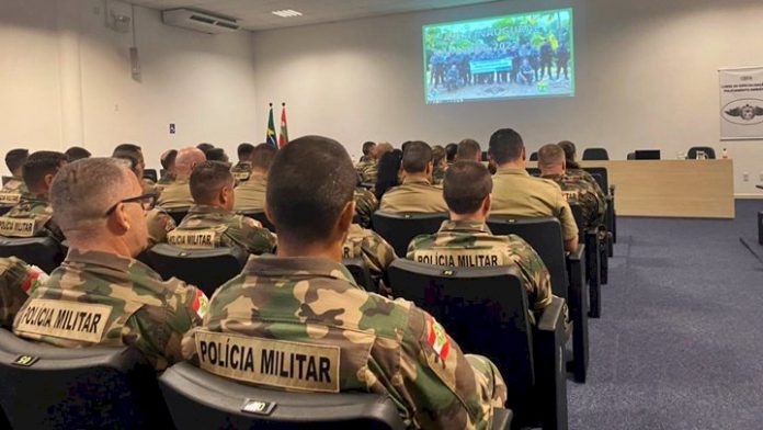 #PraCegoVer Na foto, policiais militares veem um vídeo sentados em um auditório