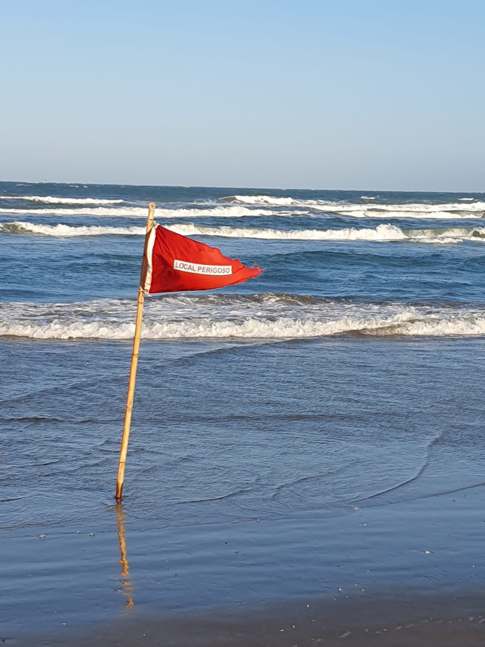 Bandeira triangular vermelha, com inscrição Local Perigoso, em branco,  indica risco aos banhistas por causa das correntes de retorno das águas.